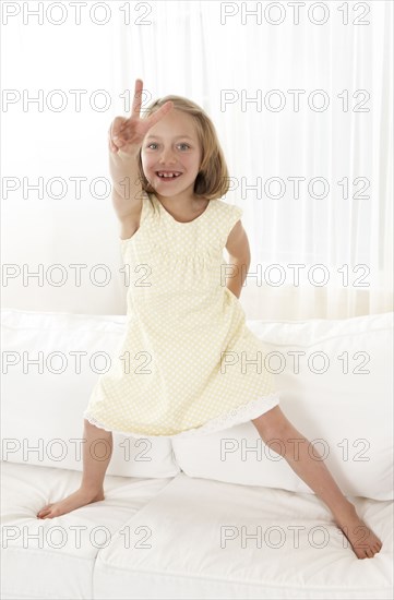 Caucasian girl standing on sofa gesturing peace sign