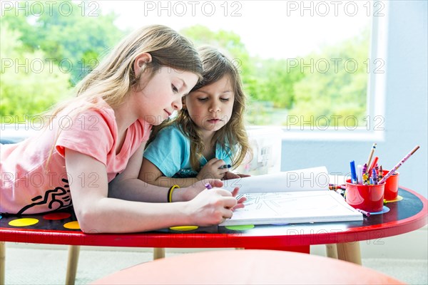 Caucasian sisters drawing at table in playroom