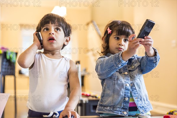Brother and sister playing with cell phone and remote control