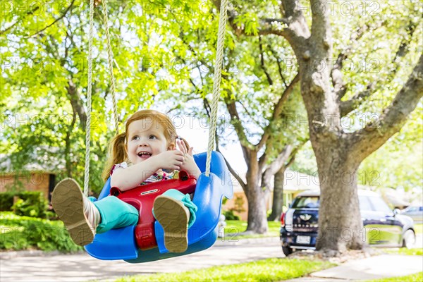 Caucasian girl playing on swing in front yard