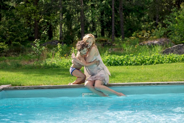 Mother hugging son at swimming pool in backyard