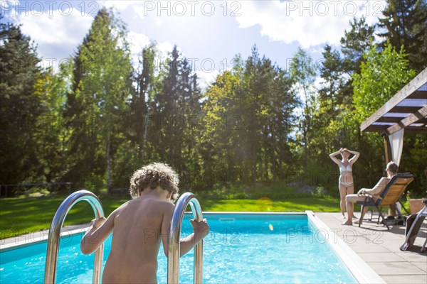 Boy climbing into swimming pool in backyard