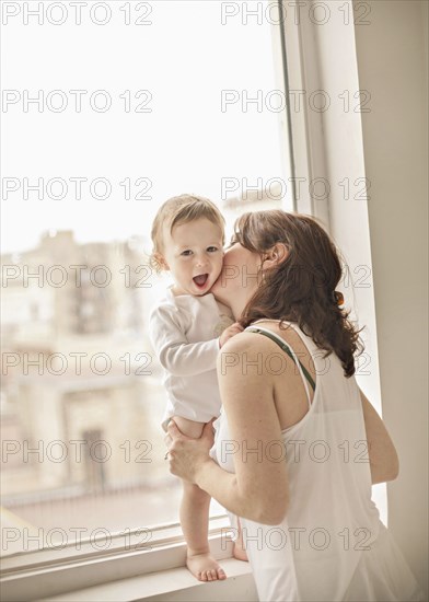 Caucasian mother kissing baby in window