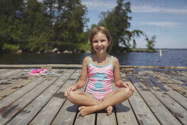 Caucasian girl sitting on wooden dock over lake