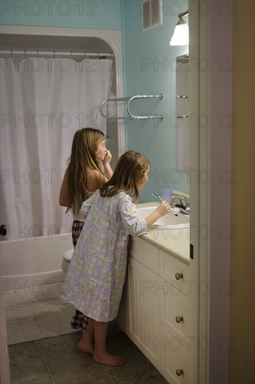 Caucasian sisters brushing teeth in bathroom