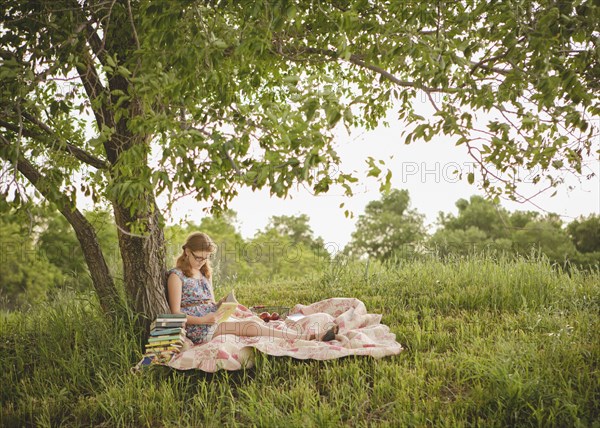 Caucasian girl reading book under tree in field