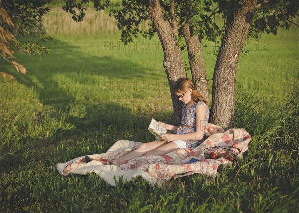 Caucasian girl reading book under tree in field