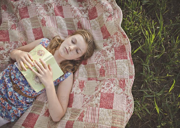 Caucasian girl sleeping with book on blanket