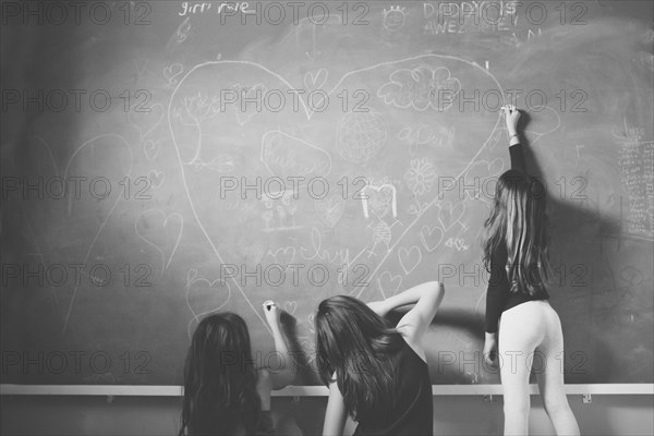 Caucasian girls drawing on classroom chalkboard