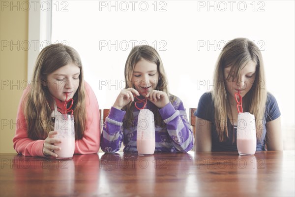 Caucasian girls drinking milk with curled straws at table