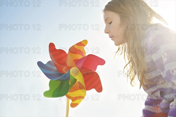 Caucasian girl playing with pinwheel under blue sky