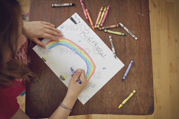 Caucasian girl drawing rainbow with crayons on table