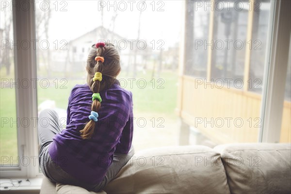 Caucasian girl looking out living room window