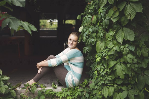 Caucasian teenage girl sitting at ivy wall