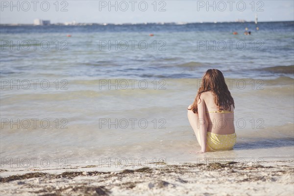 Caucasian teenage girl sitting in waves on beach