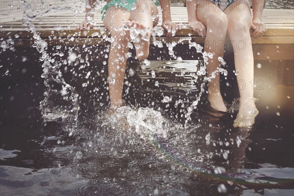 Caucasian girls splashing in lake from wooden dock