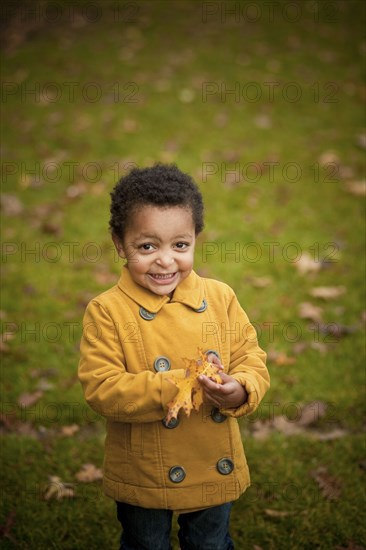 Smiling girl wearing yellow coat holding autumn leaves