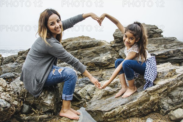 Hispanic mother and daughter making heart shape in tide pools