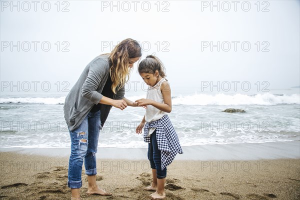 Hispanic mother and daughter standing barefoot on beach