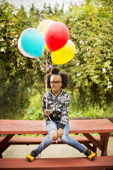 Black girl holding bunch of balloons on picnic table