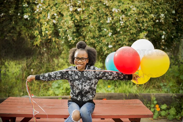 Black girl holding bunch of balloons on picnic table