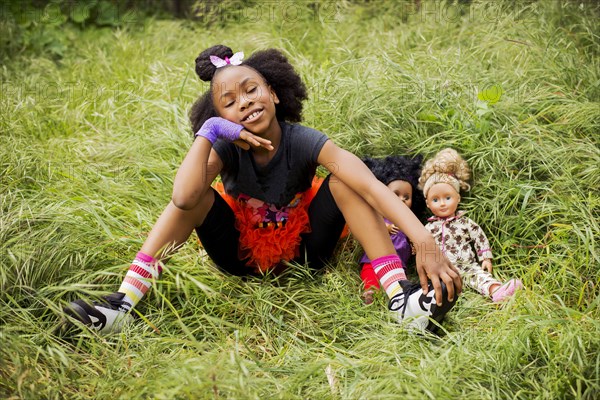 Black girl playing with dolls in tall grass