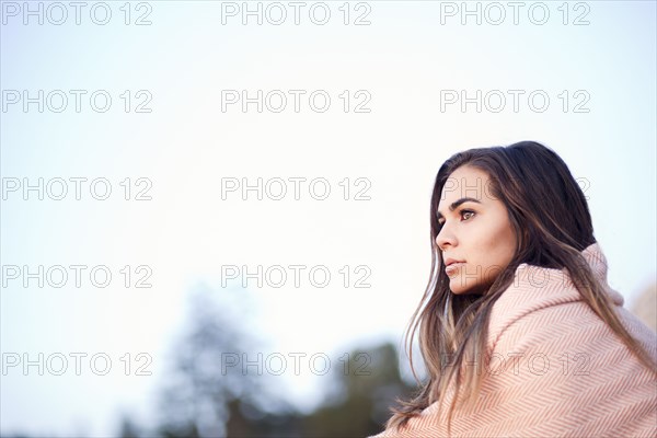 Mixed race woman wrapped in blanket under blue sky