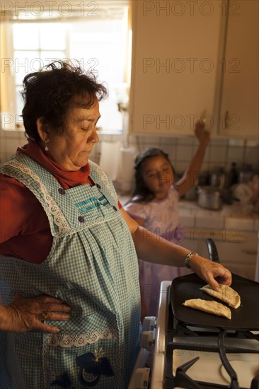 Hispanic woman cooking for granddaughter in kitchen