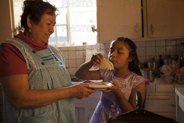 Hispanic woman cooking for granddaughter in kitchen