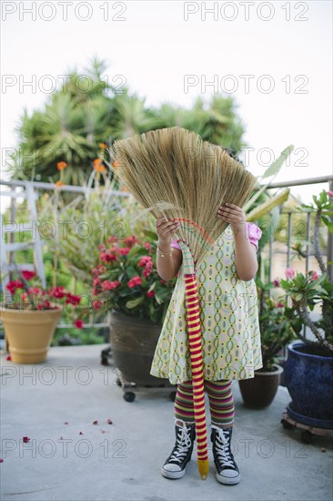 Girl hiding face on patio with broom