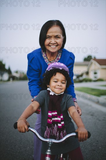 Grandmother teaching granddaughter to ride bicycle on suburban street