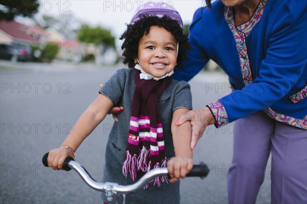 Grandmother teaching granddaughter to ride bicycle on suburban street