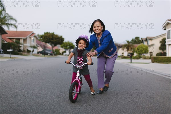 Grandmother teaching granddaughter to ride bicycle on suburban street