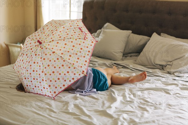 Caucasian girl playing with umbrella on bed