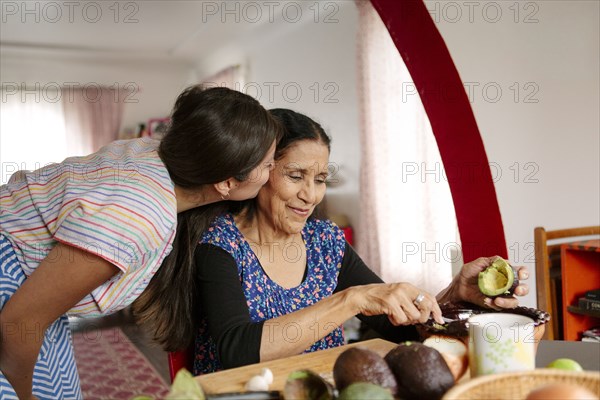 Woman kissing grandmother cooking in kitchen