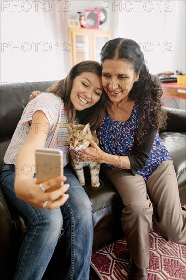 Grandmother and granddaughter taking selfie with cat on sofa