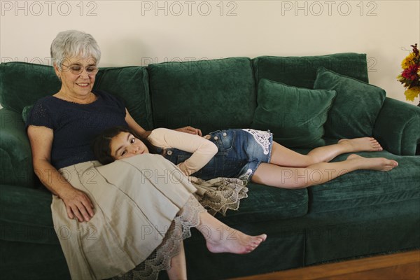 Grandmother and granddaughter sitting on sofa in living room