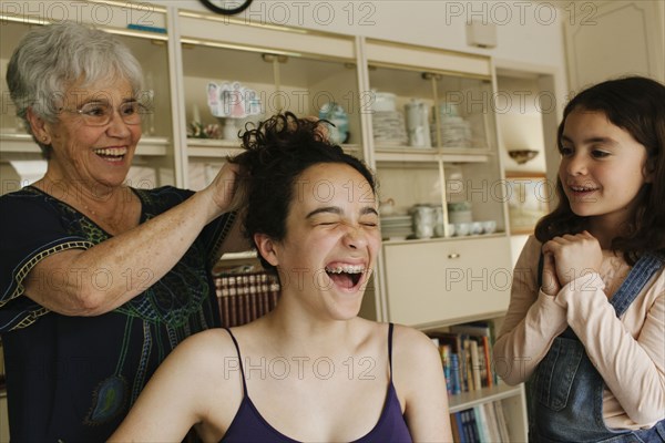Grandmother styling hair of granddaughter in dining room