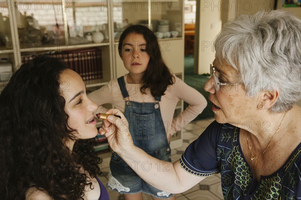 Grandmother applying lipstick to granddaughter in dining room