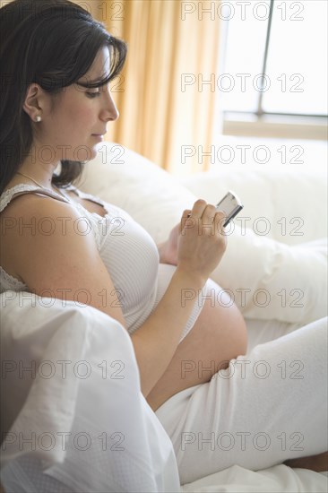 Pregnant woman using cell phone on sofa