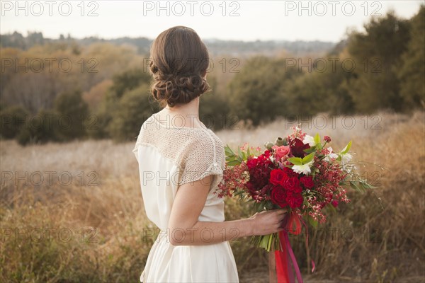 Bride holding bouquet on rural hilltop