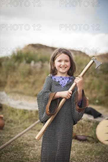 Caucasian girl in chain mail carrying hatchet in backyard