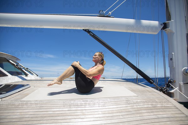 Caucasian woman practicing yoga on sailboat deck