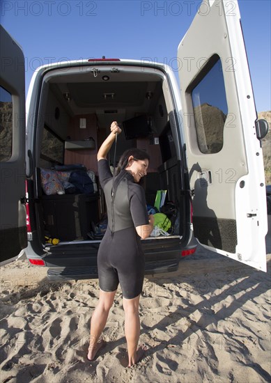 Hispanic surfer zipping wetsuit on beach