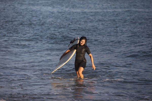 Hispanic surfer carrying surfboard in ocean