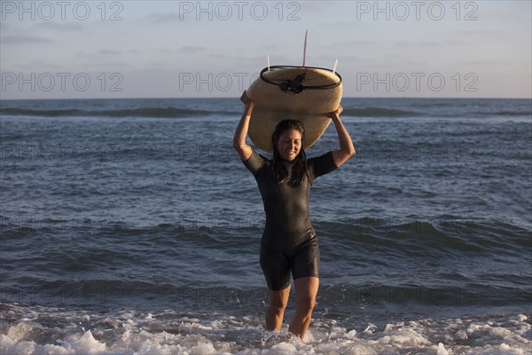 Hispanic surfer carrying surfboard in ocean