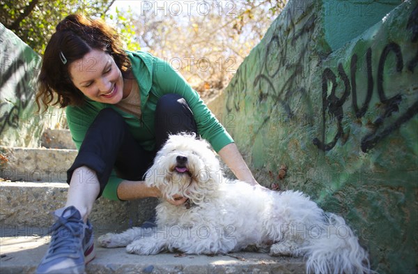 Caucasian woman petting dog on staircase with graffiti