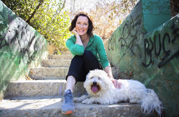 Caucasian woman petting dog on staircase with graffiti