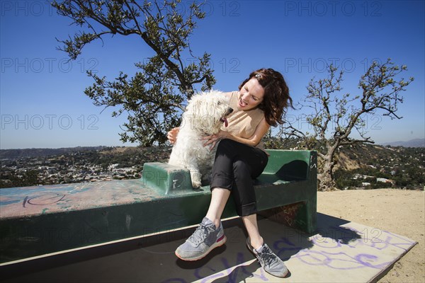 Caucasian woman petting dog on hilltop bench