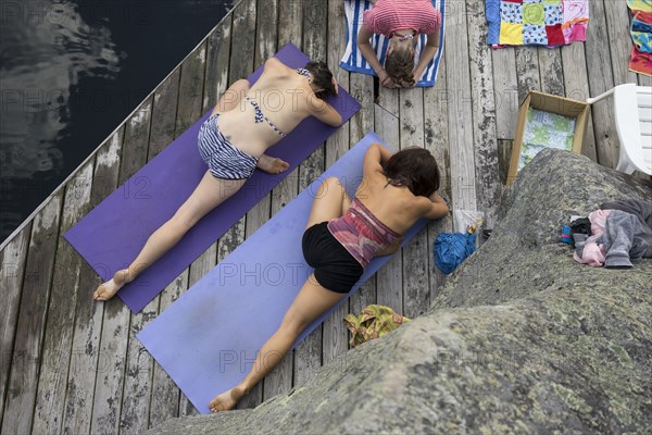 Women practicing yoga on wooden dock